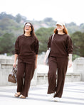 Load image into Gallery viewer, Two women walking outdoors on a crosswalk wearing matching dark brown sweatshirt and wide-leg pants sets. One wears a black cap and white sneakers, and the other wears glasses and sandals.